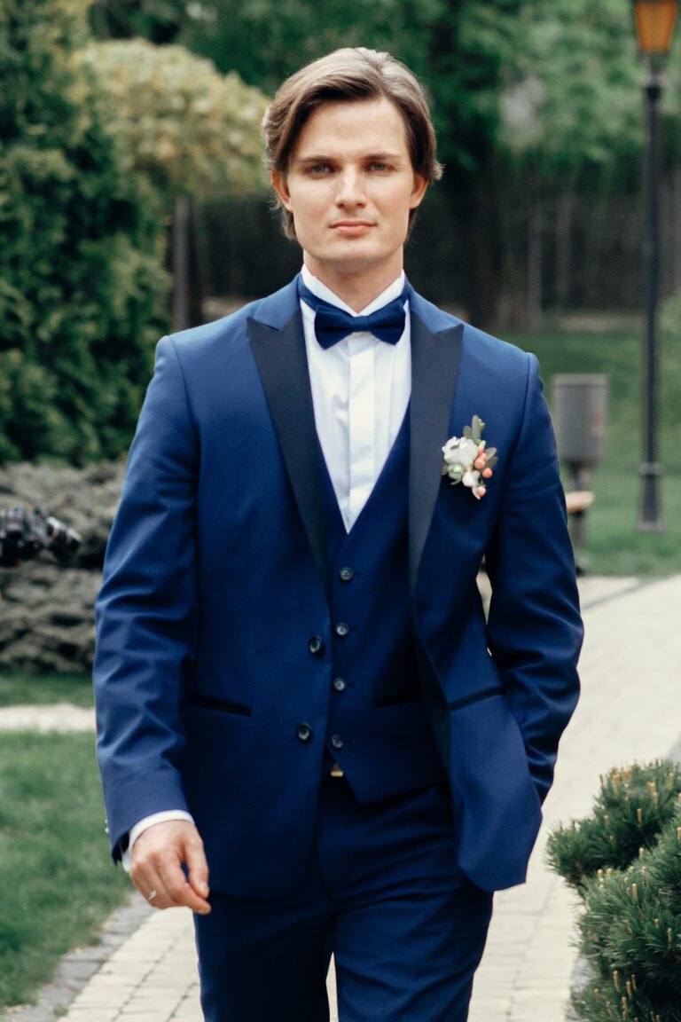 Handsome stylish groom in blue suit walking on a road in the park, newlywed man in elegant clothing posing outdoors, confident businessman portrait